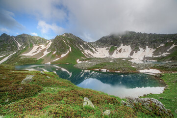 Lake with clear water in a mountain valley. Mountains are reflected in the water.