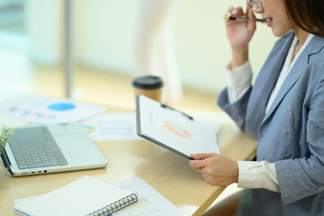 Cropped shot of focused businesswoman in eyeglasses analyzing financial graph at working desk