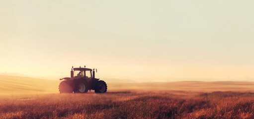 Naklejka premium Tractor Working In Misty Morning Field With Golden Light, Agricultural Scene