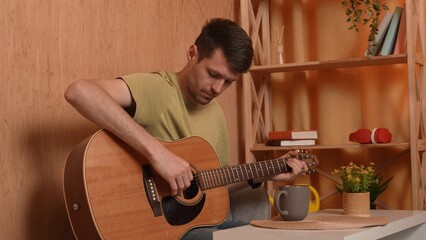 Adult man guitarist sitting in the room playing acoustic guitar, composing melody, fingering...