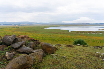 Part of Bareti lske is surrounded by fields of faded grass. Huge rocks with brown lichen in the foreground