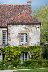 Façade d'une grande bâtisse ancienne en pierre, avec des fenêtres blanche et une vigne grimpante.