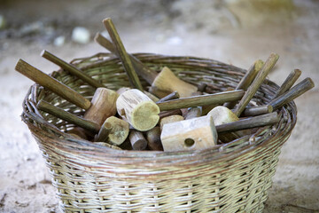 Grand panier en osier posé au sol, contenant beaucoup de petits marteau en bois. Différentes...