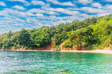 scenic summer landscape of beautiful sea shore with water vawes in bay, green forest on isle rock and nice cloudy sky on background