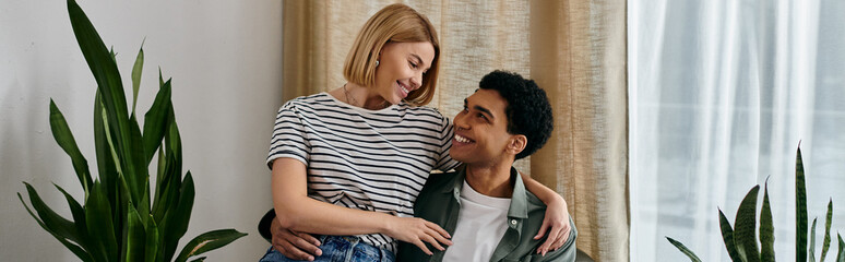 A young, multicultural couple enjoys a cozy evening in their modern apartment, surrounded by plants and natural light.