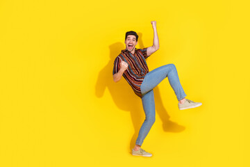 Full size photo of nice young man raise fists empty space wear shirt isolated on yellow color background