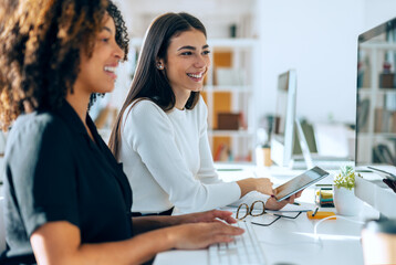 Two attractive business women talking and working with computer and digital tablet in coworking...