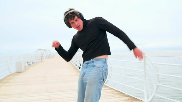 Dancing guy on beach, stoned listen new music in headphones, against the backdrop of tropical ocean and clouds.