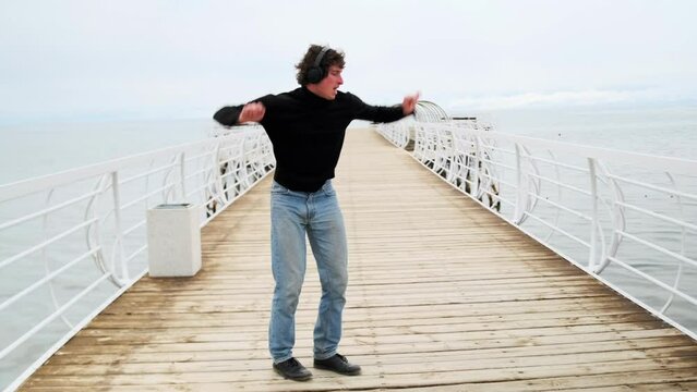 Young partygoer dancing alone in the morning after a party on a lake bridge in cloudy weather. Happy weekends and holidays.