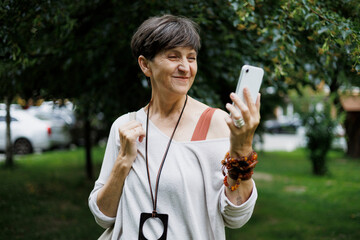 Joyful mature woman using smartphone on urban street