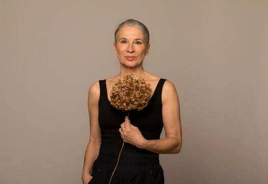 Woman with hands in pockets holding withered flower against brown background