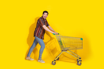 Full length portrait of nice young man push market trolley wear shirt isolated on yellow color...