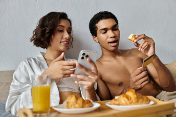 A young interracial couple enjoys a cozy morning together in their bedroom, sharing a meal and spending quality time together. - Powered by Adobe