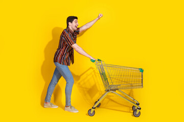 Full length portrait of nice young man raise fist trolley empty space wear shirt isolated on yellow...