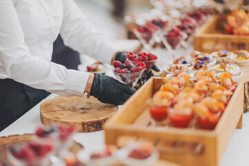 hands of a waiter prepare food for a buffet table in a restaurant. caterer arranges array of...