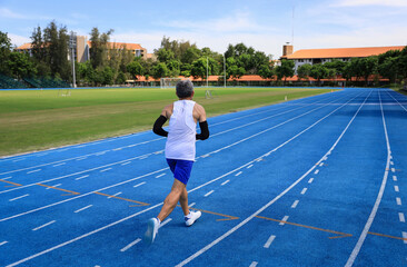 Obraz premium Senior Asian athlete is practicing running in the professional blue track for professional exercise, sport training workout and healthy for longevity concept
