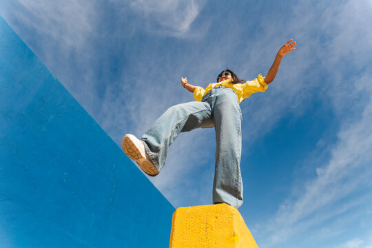 Carefree woman balancing on retaining wall in front of sky