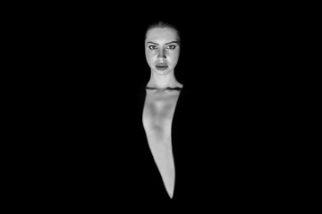 A black and white portrait of a woman looking directly at the camera, her expression is neutral and...