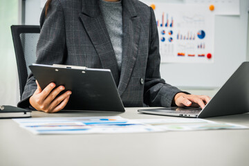 A businesswoman works diligently at her desk, reviewing financial documents and analyzing...