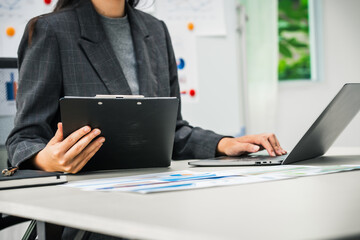 A businesswoman works diligently at her desk, reviewing financial documents and analyzing investment data. She ensures accuracy and efficiency in financial calculations and audit processes.