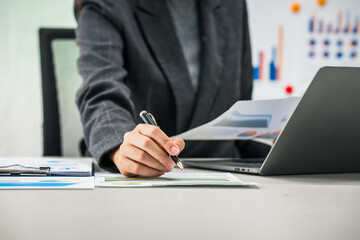 A businesswoman works diligently at her desk, reviewing financial documents and analyzing investment data. She ensures accuracy and efficiency in financial calculations and audit processes.