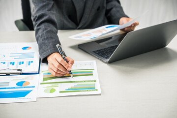 A businesswoman works diligently at her desk, reviewing financial documents and analyzing...