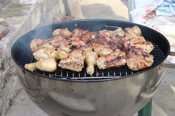 Chicken drumsticks are cooked over a fire on a barbecue grill. 