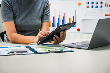A businesswoman works diligently at her desk, reviewing financial documents and analyzing...