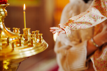 Naklejka premium A small child's hand reaches for a candle in a church candlestick. The Sacrament of Baptism of Children in the Orthodox Church. Faith in God.