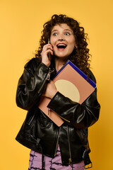 A young woman with curly hair poses in a black leather jacket against a vibrant yellow background.