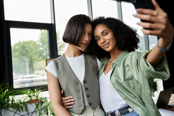 Two women, a lesbian couple, pose for a selfie in their office.