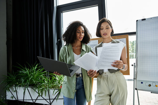 Two women working together in an office, reviewing documents. - Powered by Adobe