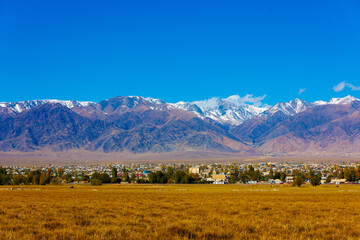 Small Kyrgyz town Balykchy cityscape in front of massive mountain ridge at sunny autumn afternoon