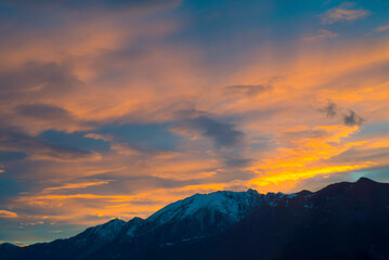 Fototapeta premium Sunset over Snow Capped Mountain Peak with Orange Clouds in Locarno, Ticino, Switzerland.