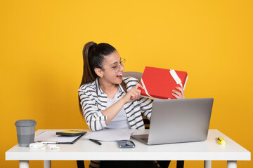 Holding present box, excited young woman  office employee business worker holding present box. Caucasian freelancer lady wondering about gift excitement during work hour. Yellow background, copy space