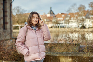 Young beautiful pretty tourist girl in warm hat and coat with backpack walking at cold autumn in Europe city enjoying her travel in Bietigheim-Bissingen, Deutschland. Outdoor portrait of young tourist