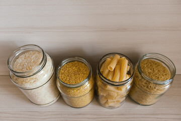 Buckwheat, pasta, bulgur and rice in glass jars on a wooden table. View from above.