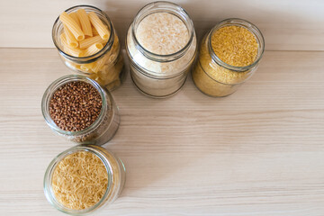 Buckwheat, pasta, bulgur and rice in glass jars on a wooden table. View from above.