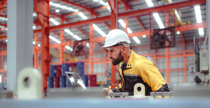 Industrial engineer in safety helmet uniform jacket working in heavy steel engineering factory. Technician manager worker inspector using laptop in metalwork product manufacturing facility workplace