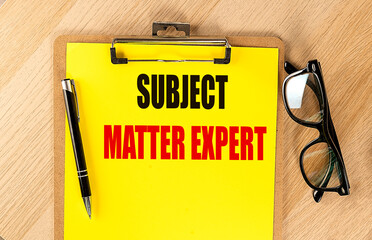 SUBJECT MATTER EXPERT text on yellow paper on clipboard with pen and glasses