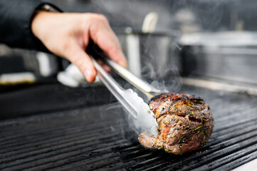 Close-up of a hand flipping a seasoned steak on a grill, smoke rising.