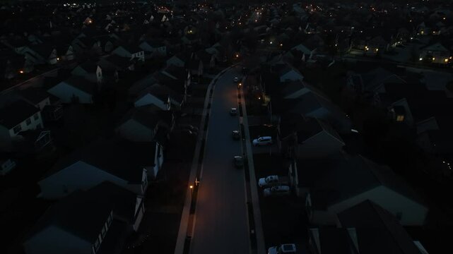 Lights illuminate large houses in upscale neighborhood in America at night. Aerial dolly forward shot of homes in development at dark.