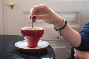 kawa w czerwonej stylowej filiżance mieszana łyżeczką trzymaną w dłoni
