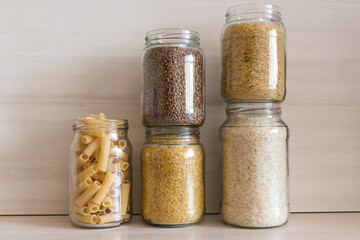 A row of glass jars filled with buckwheat, pasta, bulgur and rice. Eco packaging for cereals.