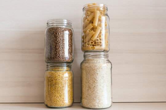 A row of glass jars filled with buckwheat, pasta, bulgur and rice. Eco packaging for cereals.