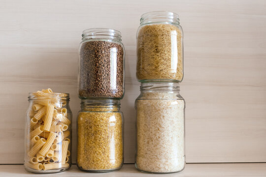A row of glass jars filled with buckwheat, pasta, bulgur and rice. Eco packaging for cereals.