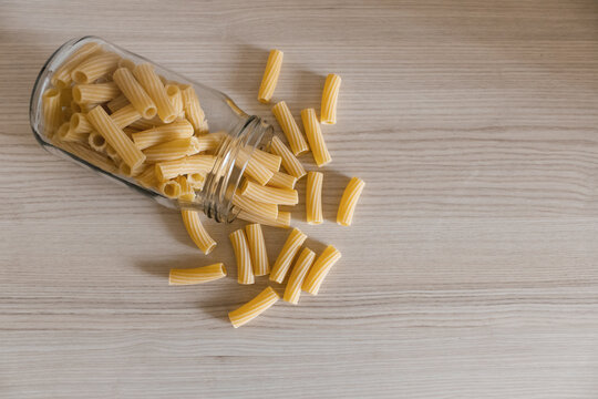 Glass jar with pasta on a light wooden table.