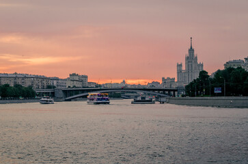 Obraz premium Moscow river with boats, capital city in the background, pink red sunset