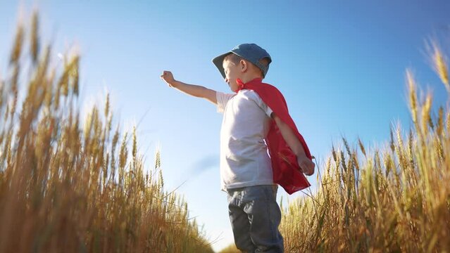Superhero and his kids play sports together after success. Growth future motivation family concept. Boy and superhero in a field of wheat. Superhero boy playing in sunset a field of wheat.