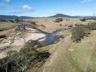 Aerial View of a winding river through a rural landscape with mountains in the background